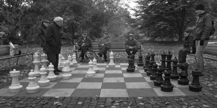 Sieben Herren an einem Freiluft-Schachspiel.