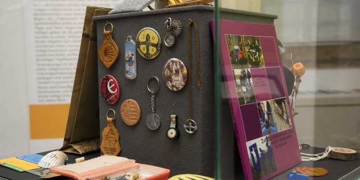 Foto: Pilgerandenken: Doch was steckt eigentlich hinter dem Phänomen des Pilgerns, welche Geschichte hat das christliche Pilgerwesen? © Stadtverwaltung Erfurt / D. Urban Vitrine, darin bunte Abzeichen und Andenken.