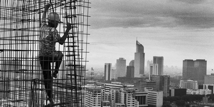 Arbeiter in Konstruktion aus Bewährungsstahl. Dahinter Großstadt mit Hochhäusern.