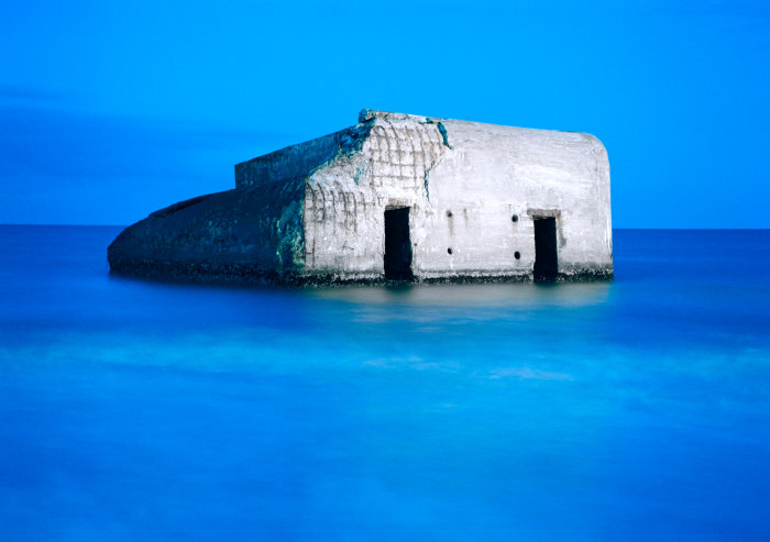 Erasmus Schröter: Bunker, WB 54, 1995, C-PrintDiasec Bild eines grauen Gebäudes, das scheinbar mitten im blauen Meer steht