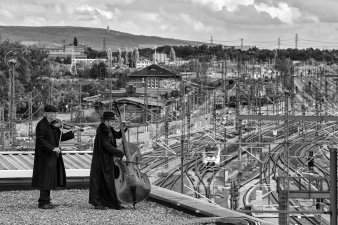 Über den Dächernn eines Bahnhofs spielen zwei Musiker auf einer Geige und einen Kontrabass