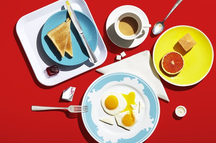 Michael Crichton & Leigh MacMillan: Breakfast in America Frühstück mit Toast, Spiegelei und Obst auf bunten Tellern arrangiert