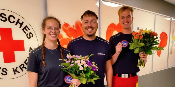 Eine Frau und zwei Männer in Sanitäterkleidung lächeln. 