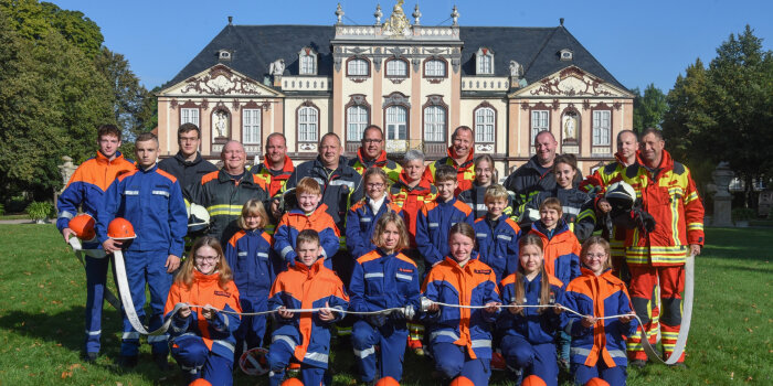 Viele Kinder und Erwachsene in Feuerwehruniformen posieren vor einem Schloss.