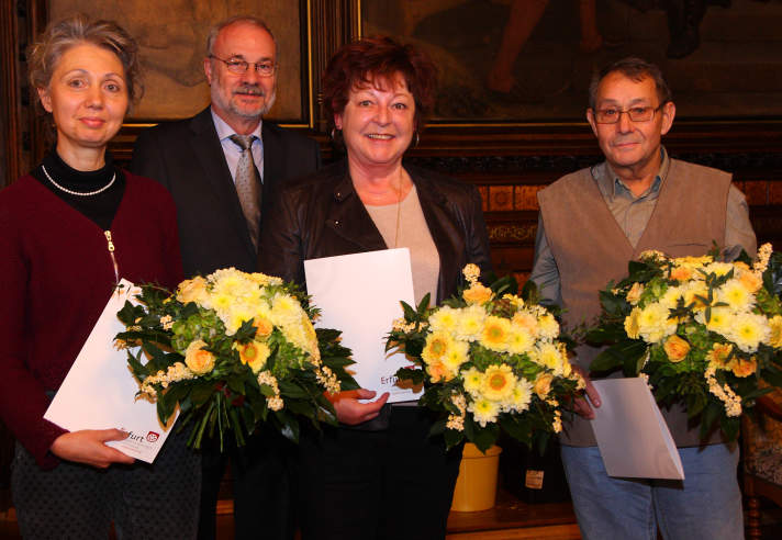 Vier Personen im Rathausfestsaal, davon drei mit gelbem Blumenstrauß