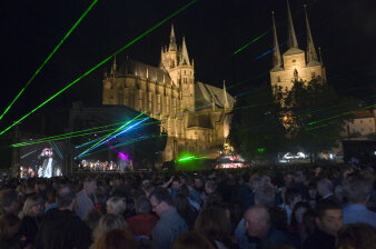 Dom und St. Severi unter dem Nachthimmel, davor auf dem Domplatz eine große Bühne, bunte Laserstrahlen und Publikum