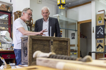 zwei Männer stehen an einer alten Holztruhe