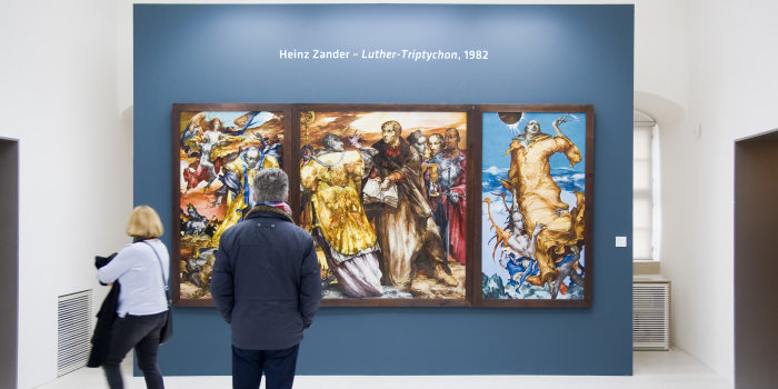 Foto: Blick in die Luther-Ausstellung. Zu sehen das Luther-Triptychon von Heinz Zander, 1982, Öl /Hartfaser, das im Auftrag des Ministeriums für Kultur der DDR anlässlich der Luther-Ehrung 1983 entstand. Befindet sich heute im Besitz des Angermuseums Erfurt © Stadtverwaltung Erfurt / D. Urban Besucher in einer Ausstellung.