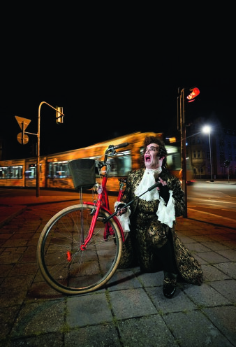 ein als König verkleideter Mann pumpt den Reifen eines roten Fahrrads auf