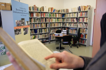 Foto: Volkskundliche Beratungs- und Dokumentationsstelle © Stadtverwaltung Erfurt Hand zeigt auf eine Fundstelle im Buch, im Hintergrund Regale