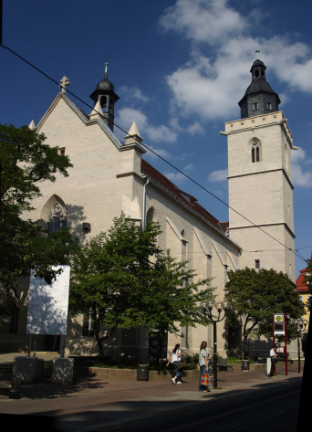 Sandsteinkirche unter blauem Himmel, davor Bäume.