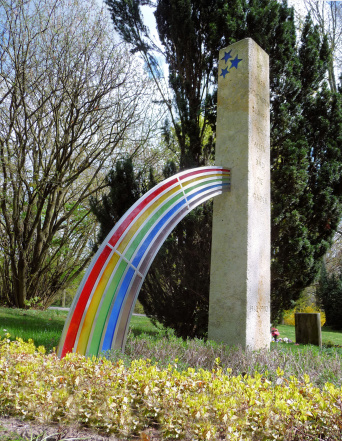 eine regenbogenbunte Stele im Grünen