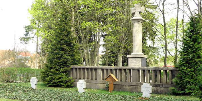 Auf einer mit Efeu bewachsenen Fläche stehen drei Granitkreuze für mit Namen von Kriegstoten. Hinter den Kreuzen steht eine steinerne Balustrade und eine Säule, die als oberen Abschluß die Darstellung des Eisernen Kreuzes trägt. 