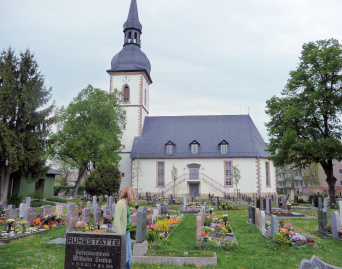 Kirche auf dem Ortsteilfriedhof Stotternheim Blick über den Friedhof zur Längsseite der hell gestrichenen Kirche. Die Fensterrahmen und Gebäudekanten sind farbig abgesetzt. In der Mitte des Kirchenschiff befinden sich zwei übereinander liegende Eingänge. Der obere wird durch eine von links und rechts kommende Treppe erreicht. dach und Turm sind mit Schiefer eingedeckt. Am Kirchturm befindet sich über dem obersten Fenster eine Kirchturmuhr.