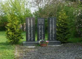 Drei schwarze Natursteinstelen auf einem Sockel, jeweils gute zwei meter hoch. darauf befinden sich die namen der Kriegsopfer. 