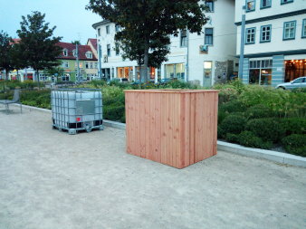 ein unverkleidetet und ein mit Holz verkleideter Wassercontainer