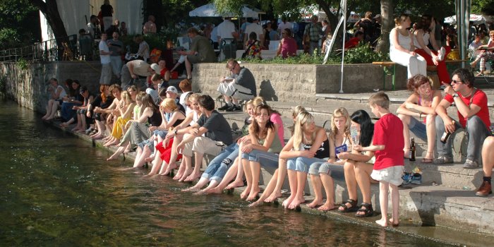 Besucher des Krämerbrückenfestes sitzen am Ufer der Gera