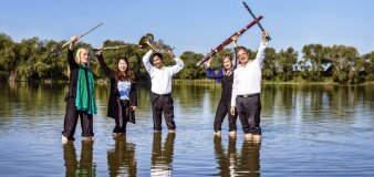 fünf Leute mit Blasinstrumenten mit den Füßen im Wasser eines Sees stehend