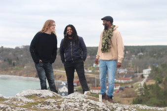 Foto: Freedoms Trio © Magdalena Stromgren drei Männer auf einem Berg und im Hintergrund das Meer und eine Siedlung