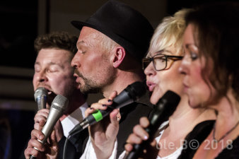 Foto: Vocalquartett © Ole Bechert zwei Sängerinnen und zwei Sänger singen vor dunklem Hintergrund in ihre Mikrofone
