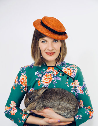 Foto: Erna Rot © Florian Brückner lächelnde Frau im grünen Blumenkleid und rotem Hut mit Kaninchen auf dem Arm