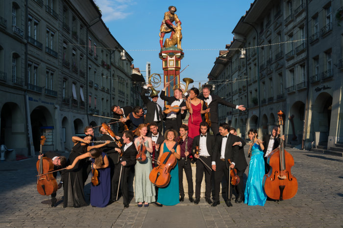 Die Orchestermitglieder mit ihren Instrumenten an einer Säule in einer historischen Altstadt