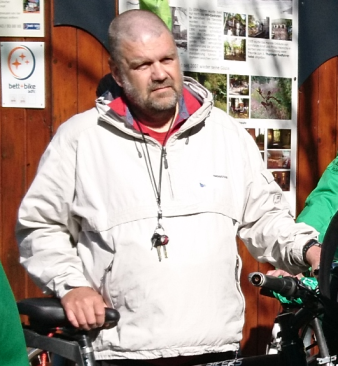 Auf dem Foto ist ein Mann zu sehen, der neben einem Fahrrad steht und dies festhält.