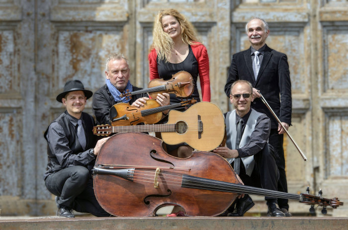 fünf Musiker mit ihren Instrumenten vor einem rostogen Tor