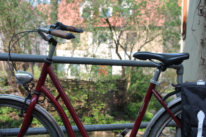 rotes Fahrrad mit Fahrradtasche angelehnt an einem Geländer 