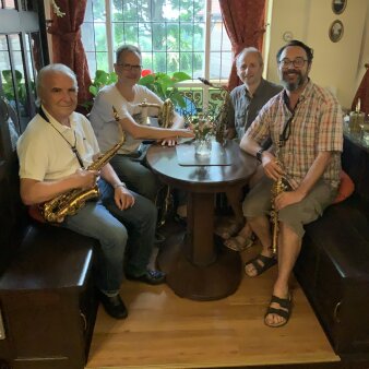 vier sitzende Männer an rundem Tisch mit Instrumenten