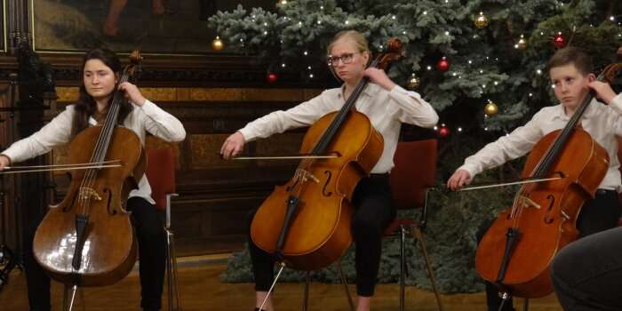 3 junge Cellospieler vor dem Weihnachtsbaum im Rathausfestsaal.