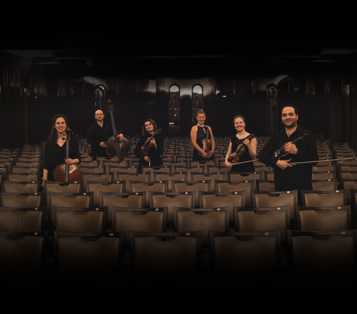 6 Musiker mit ihren Instrumenten zwischen den Besucherstühlen eines Konzerthauses