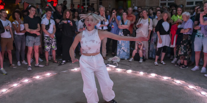 Tanzende Frau in einem Lichtkreis mit Zuschauern herum 