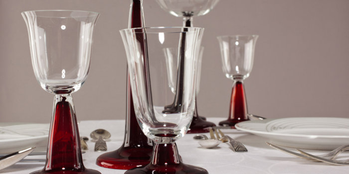 Peter Behrens, Gläser, farblos, mit rot gefärbtem Stängel und Fuß, Porzellanservice und Besteck, 1901 Fünf filigrane Gläser auf weißem Tischtuch, zwei Teller und verschiedene Besteckteile