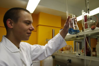 Ein Mitarbeiter steht im Labor und schwenkt eine blaue Flüssigkeit in einem Gefäß