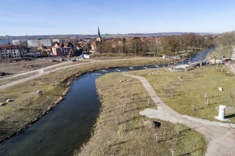 Luftaufnahmer einer von einem Fluss durchzogenen Parklandschaft, die teilweise Baustelle ist