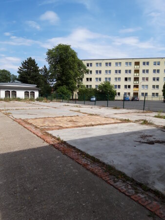 eine leere Platzfläche, im Hintergrund ein mehrstöckiges Haus