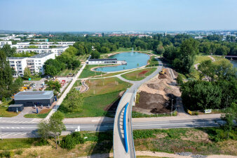 Luftaufnahme einer Parklandschaft mit Teich, im Vordergrund eine Straße mit Brücke