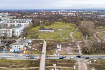 Luftaufnahme einer Straße mit Brücke und einer sich anschließenden Parklandschaft, links ein Neubaugebiet