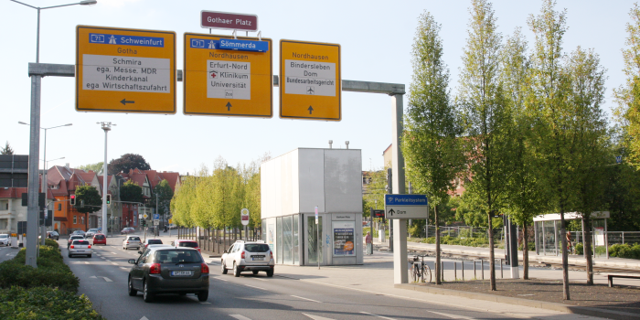 Platz/Straße mit Schilderbrücke, Pkws und Haltestelle