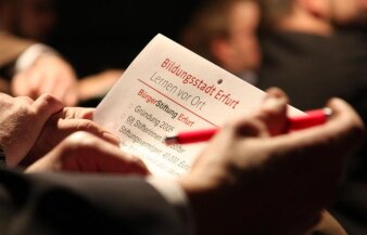 Ein Mann hält einen Zettel mit der Aufschrift "Bildungsstadt Erfurt - Lernen vor Ort" in der Hand.