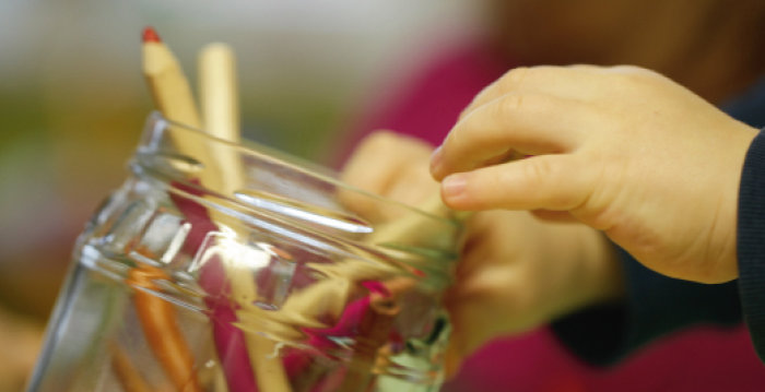 Glas mit diversen Buntstiften wird von zwei Kinderhänden gekippt.