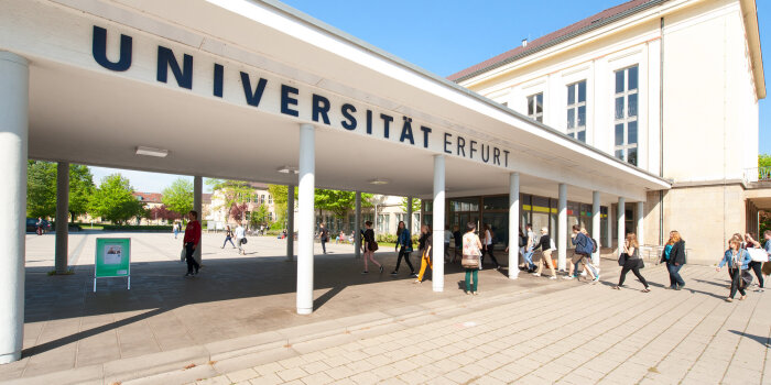 Mehrere Menschen vor einem weißen Portal, auf dem „Universität Erfurt“ steht. 