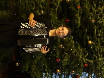 Schülerin mit Akkordeon vor dem Weihnachtsbaum