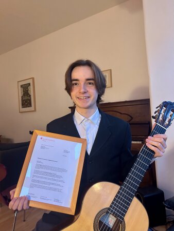 junger Gitarrist hält Gitarre und Urkunde für Stipendium