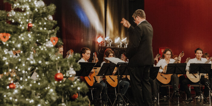 ein Mann digirigierte junge Gitarrenspielerinnen und -spieler, im Vordergrund ein Weihnachtsbaum