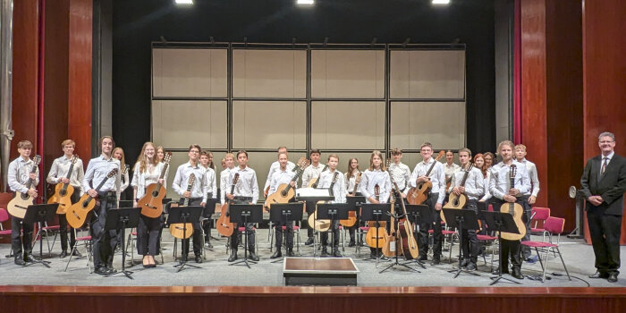 mehrere schwarz-weiß gekleidete junge Musikerinnen und Musikern stehen mit Gitarren auf der Bühne