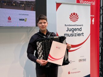 Schüler mit Akkordeon und Urkunde neben einem Jugend muisziert Banner