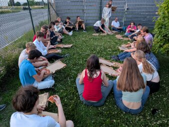 Schülergruppe sitzen im Kreis auf einer Wiese und isst Pizza