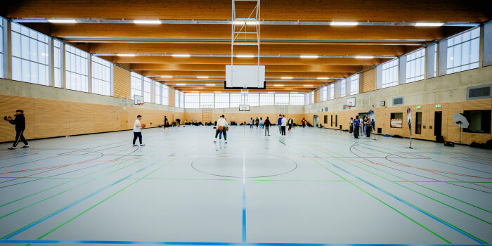 mehrere Menschen spielen Basketball in einer großen Turnhalle